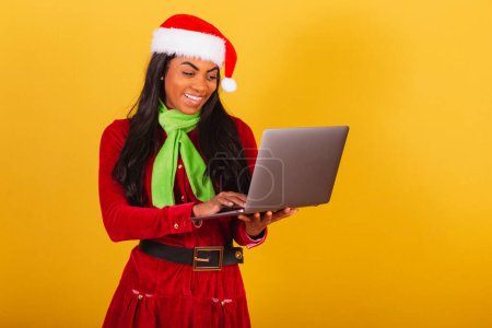 Photo for Beautiful black Brazilian woman, dressed in Christmas clothes, Santa Claus, holding notebook. - Royalty Free Image