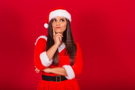Foto de Hermosa mujer brasileña vestida con ropa de Navidad, Santa Claus. duda, cuestionamiento, pensamiento. - Imagen libre de derechos