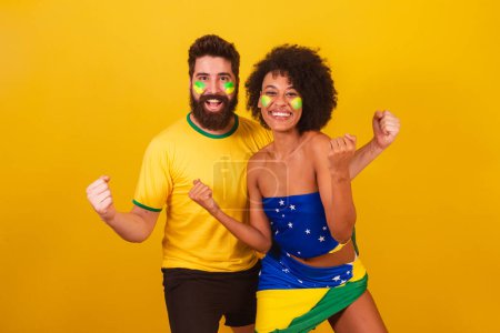 Téléchargez les photos : Couple de fans de football brésilien, habillé dans les couleurs du brésil, femme noire, homme caucasien. crier oui, célébrer la victoire - en image libre de droit