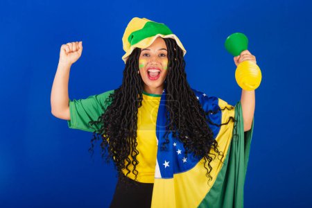 Photo for Young black Brazilian woman, soccer fan. with flag and accessories, celebrating goal. - Royalty Free Image