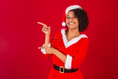 Téléchargez les photos : Belle femme brésilienne noire, habillée en Père Noël claus, maman claus, présentant le produit ou des informations sur le côté - en image libre de droit