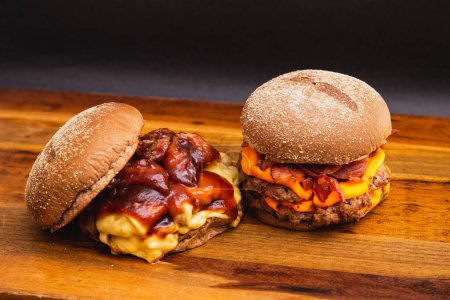 Foto de Dos hamburguesas hechas a mano en una tabla de madera, hechas con carne de res. Tocino, queso y salsa barbacoa. - Imagen libre de derechos