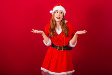 Photo for Beautiful Brazilian red-haired woman, dressed in Christmas clothes, Santa Claus. expression of doubt. - Royalty Free Image