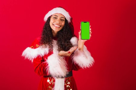 Photo for Beautiful brazilian black woman, dressed as santa claus, christmas clothes. holding cell phone, with chroma screen. - Royalty Free Image