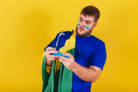 Foto de Brasileño caucásico hombre, ventilador de fútbol de Brasil, jugando juego por teléfono celular. - Imagen libre de derechos