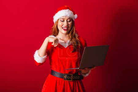 Foto de Hermosa brasileña pelirroja, vestida con ropa de Navidad, Santa Claus. sosteniendo el cuaderno. Wow, increíble, increíble. - Imagen libre de derechos