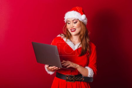 Téléchargez les photos : Belle femme rousse brésilienne, vêtue de vêtements de Noël, le Père Noël. tenant un carnet. - en image libre de droit
