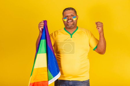 Foto de Hombre negro brasileño, fanático del fútbol de Brasil. mantener la bandera lgbt - Imagen libre de derechos
