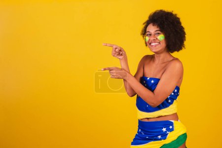 Téléchargez les photos : Jeune femme noire fan de football brésilien. présenter un produit ou des informations sur le côté - en image libre de droit