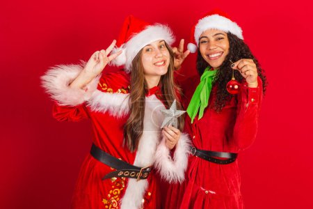 Photo for Two brazilian friends, dressed in christmas clothes, santa claus, holding christmas decoration, stars and red ball. - Royalty Free Image