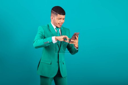 Téléchargez les photos : Homme noir brésilien, vêtu de costume et cravate verte, homme d'affaires. en utilisant un smartphone - en image libre de droit