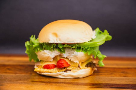 Foto de Deliciosa hamburguesa brasileña tradicional, X all. salchichas, huevo, tomate, queso y ensalada. sobre tabla de madera. - Imagen libre de derechos
