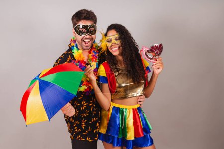 Photo for Brazilian couple, with carnival clothes. holding carnival accessories, umbrella and mask. - Royalty Free Image