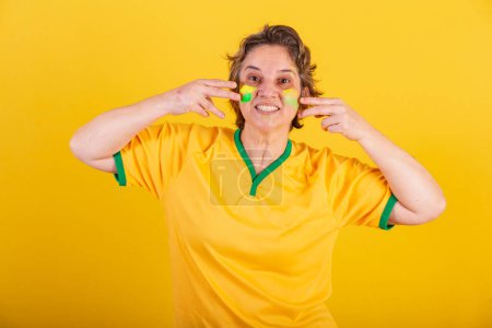 Photo for Adult adult woman, soccer fan from brazil, putting paint on her face, brazilian fans. painted face. - Royalty Free Image