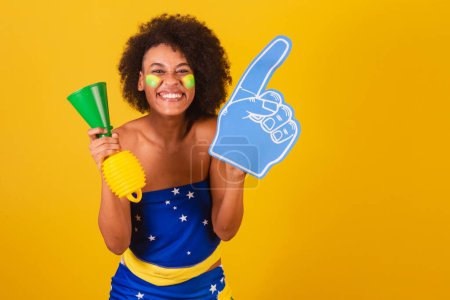 Téléchargez les photos : Jeune femme noire fan de football brésilien. avec corne et doigt de mousse, acclamant. - en image libre de droit
