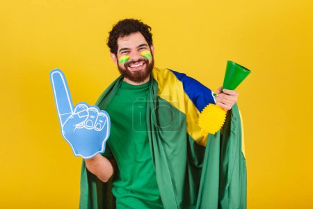 Photo for Man, brazilian, bearded, soccer fan from brazil, using foam finger and horn, celebrating in soccer match. - Royalty Free Image