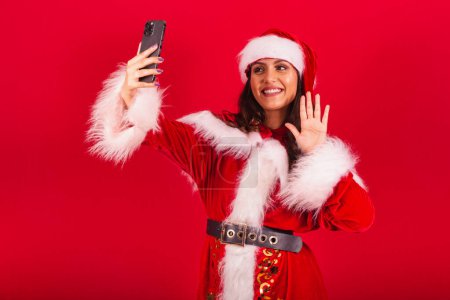 Photo for Brazilian woman dressed in Christmas clothes, Santa Claus. taking self portrait photo with smartphone. - Royalty Free Image