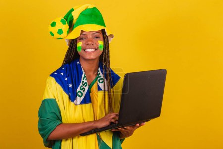 Téléchargez les photos : Femme noire jeune fan de football brésilien. utilisant ordinateur portable, internet, connecté. - en image libre de droit