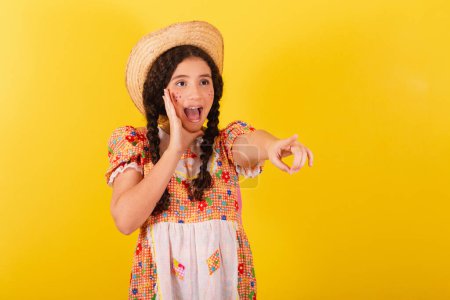 Photo for Girl wearing traditional orange clothes for festa junina. Sighting and pointing to something far away, incredible. Promotion, advertisement. - Royalty Free Image