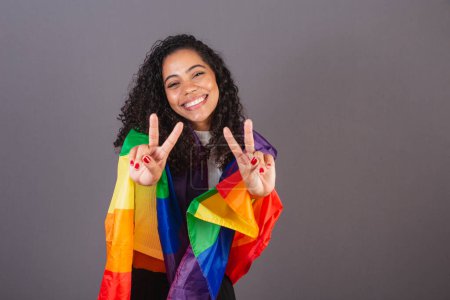 Téléchargez les photos : Jeune femme noire brésilienne, signe de paix et d'amour, militantisme avec le drapeau LGBT, diversité. - en image libre de droit