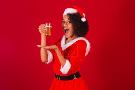Photo for Beautiful black brazilian woman, dressed as santa claus, mama claus, holding glass of beer - Royalty Free Image