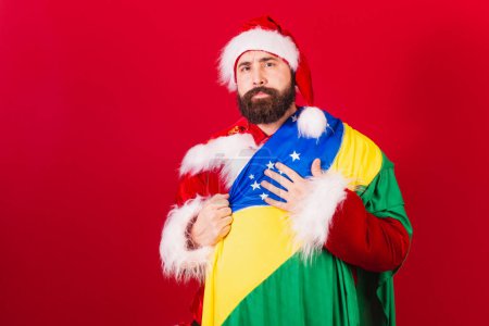 Téléchargez les photos : Santa claus brésilien jeune homme caucasien. avec drapeau brésilien. optimiste. - en image libre de droit
