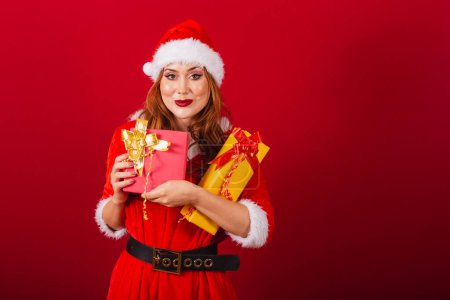 Téléchargez les photos : Belle femme rousse brésilienne, vêtue de vêtements de Noël, le Père Noël. étreignant deux cadeaux. - en image libre de droit