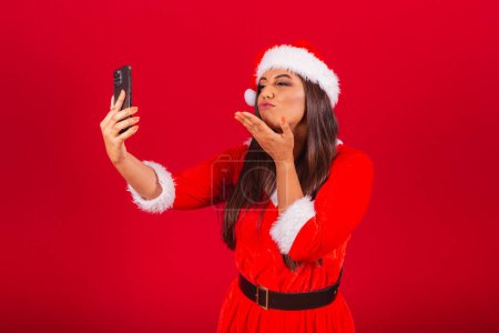Téléchargez les photos : Belle Brésilienne vêtue de vêtements de Noël, le Père Noël. tenir un appel vidéo smartphone. - en image libre de droit