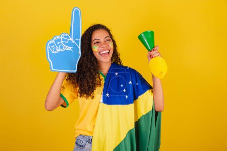 Foto de Joven brasileña negra, fanática del fútbol. con bandera y accesorios, vitoreando. - Imagen libre de derechos