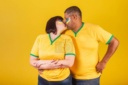Téléchargez les photos : Couple, femme rousse et homme noir, fans de football brésilien. donnant baiser. - en image libre de droit