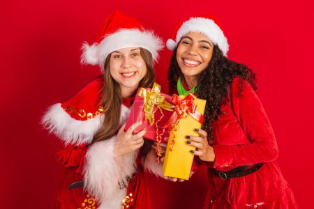 Photo for Two brazilian friends, dressed in christmas clothes, santa claus, exchanging christmas gifts. - Royalty Free Image