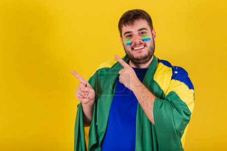 Photo for Brazilian caucasian man, soccer fan from brazil, pointing with fingers to the left, photo for ad. - Royalty Free Image