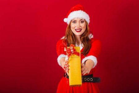 Photo for Beautiful Brazilian red-haired woman, dressed in Christmas clothes, Santa Claus. handing yellow gift to camera. - Royalty Free Image
