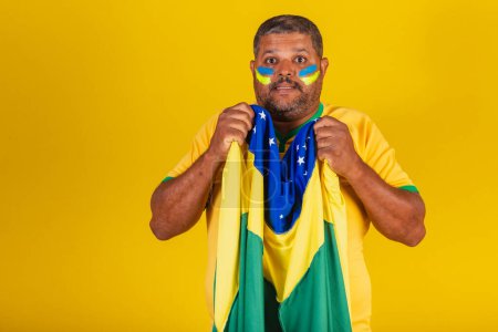 Foto de Hombre negro brasileño, fanático del fútbol de Brasil. ondeando la bandera brasileña, ansioso, nervioso. - Imagen libre de derechos