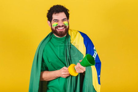 Photo for Man, brazilian, bearded, soccer fan from brazil, using his horn in a world cup match, partying, making noise. - Royalty Free Image
