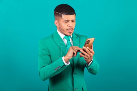 Photo for Brazilian black man, dressed in suit and green tie, Businessman. using smartphone - Royalty Free Image