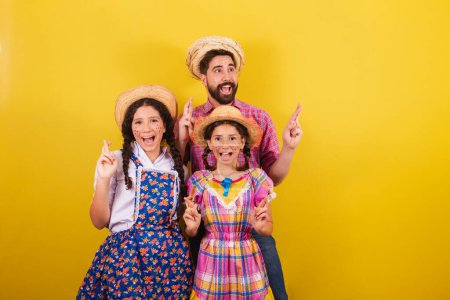 Father and daughters wearing typical clothes for the Festa Junina. with crossed fingers, twisting, wishing, hopeful. For the Arraia party