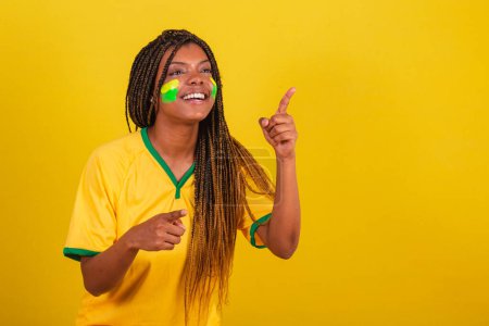 Photo for Black woman young brazilian soccer fan. pointing something far away, photo for advertising. soccer brazil. - Royalty Free Image