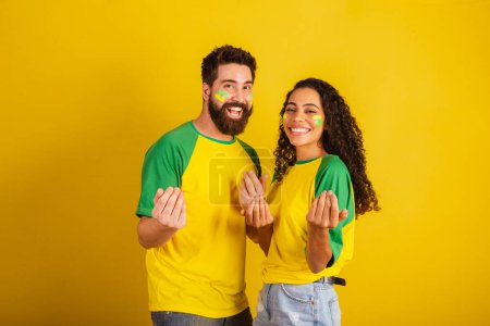Photo for Couple of brazil soccer supporters, dressed in the colors of the nation, black woman, caucasian man. inviting with hands. - Royalty Free Image