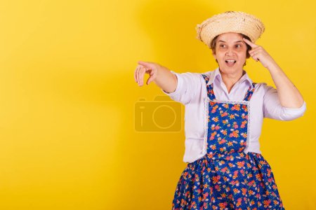 Photo for Mature woman dressed in typical Festa Junina clothes. Pointing at something in the distance, looking indicating. - Royalty Free Image