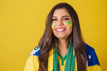 Téléchargez les photos : Femme supporter du Brésil, coupe du monde 2022, championnat de football, en utilisant le drapeau brésilien comme couverture. gros plan photo, sourire, regarder le match de football. - en image libre de droit