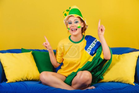 Photo for Caucasian woman, redhead, Brazilian soccer fan, Brazilian, on couch dancing - Royalty Free Image