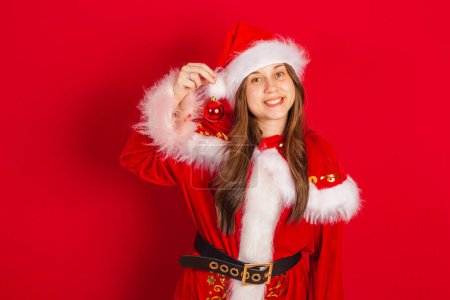 Téléchargez les photos : Caucasienne, Brésilienne en vêtements de Noël, Père Noël. Tenue d'une boule de Noël. - en image libre de droit