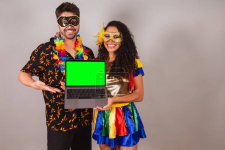 Photo for Brazilian couple, with carnival clothes. of holding notebook, programming, web. - Royalty Free Image