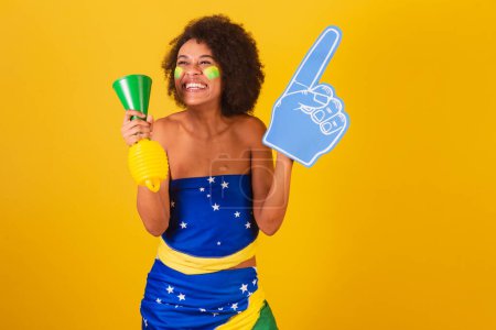 Photo for Young black woman brazilian soccer fan. with horn and foam finger, cheering. - Royalty Free Image