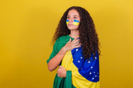 Foto de Brasileña, chica caucásica, fanática del fútbol, cantando himno nacional. Nacionalismo. - Imagen libre de derechos
