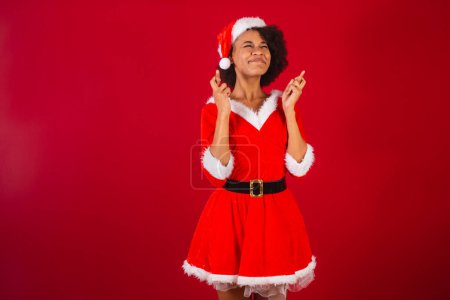 Téléchargez les photos : Belle femme brésilienne noire, habillée en Père Noël claus, maman claus, doigts croisés, souhaitant, acclamant, voulant - en image libre de droit