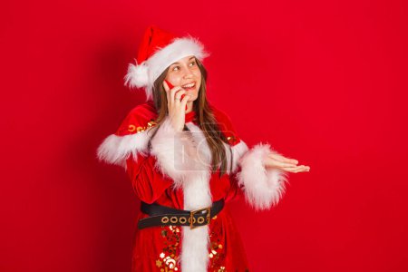 Photo for Caucasian, Brazilian woman in Christmas clothes, Santa Claus. in voice call by smartphone. - Royalty Free Image