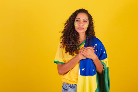 Téléchargez les photos : Jeune Brésilienne noire, fan de foot. avec drapeau brésilien. chanter l'hymne national. - en image libre de droit