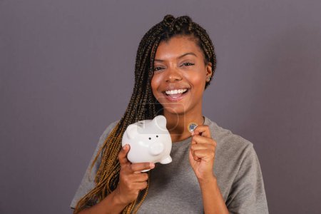 Foto de Joven mujer afro brasileña sosteniendo alcancía y moneda, concepto de economía, finanzas, ahorro. - Imagen libre de derechos